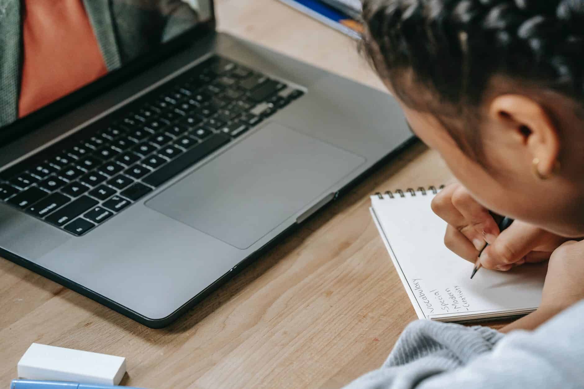 ethnic girl studying online with laptop and writing notes